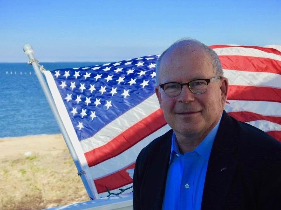 Andy Baan standing in front of an American flag on the Virginia Beach waterfront